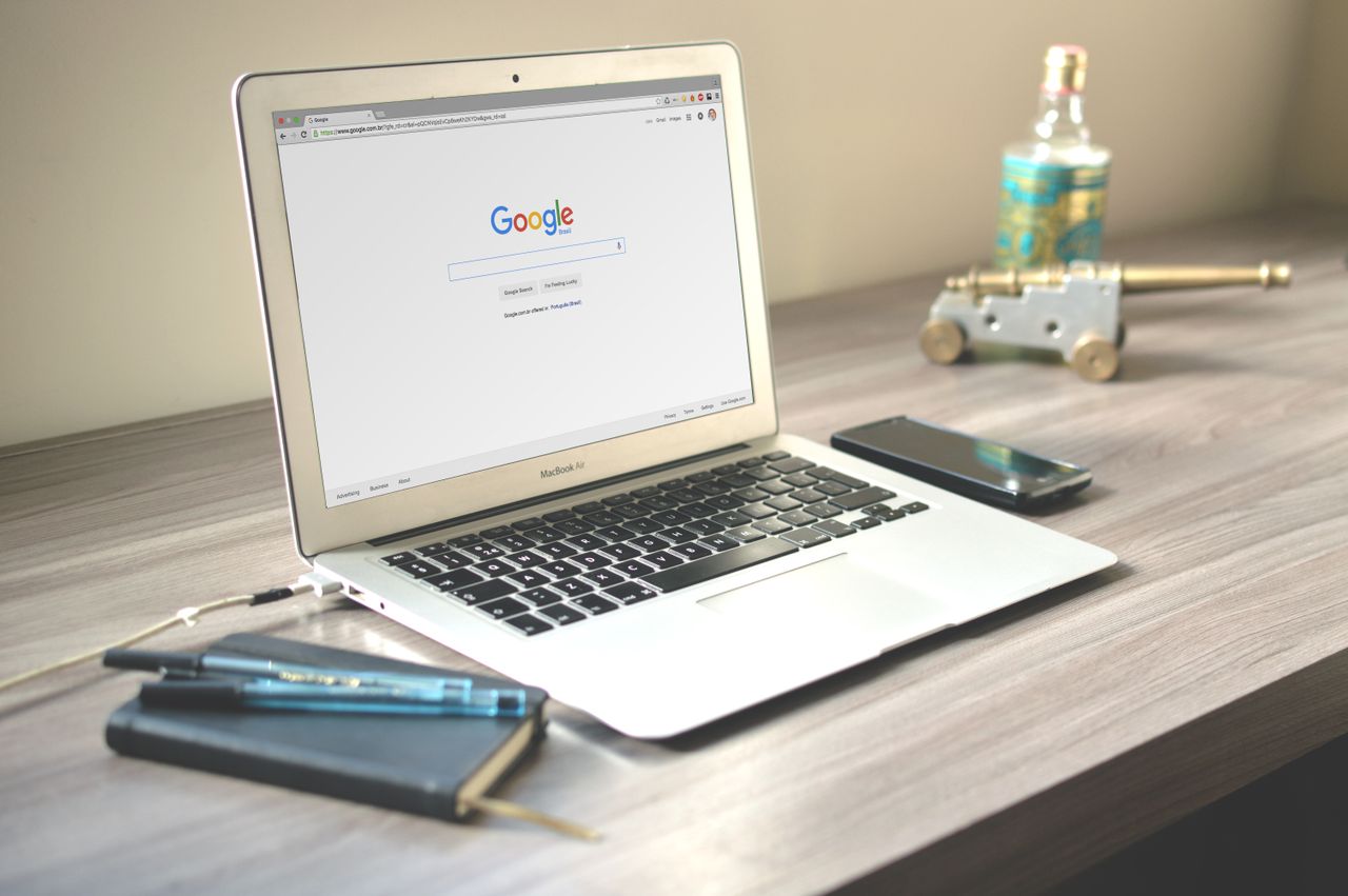 A tidy workspace with a laptop showing Google search, a smartphone, and a notebook on a wooden desk.